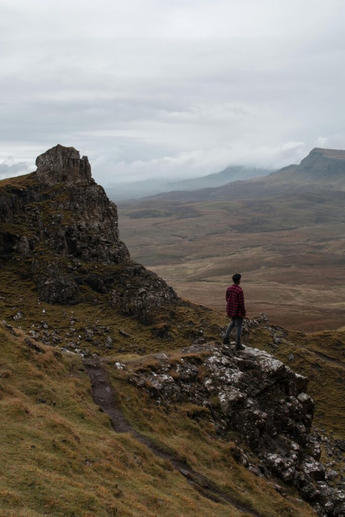 Man stands on cliff overlooking the rugged landscape of Isle of Skye, Scotland.